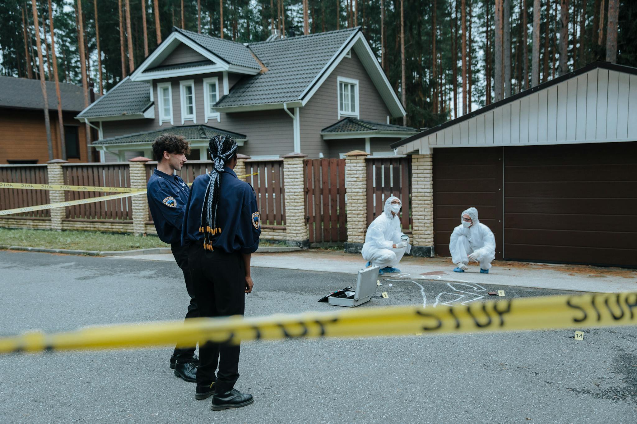 Police and forensic experts examining a crime scene in front of suburban houses.